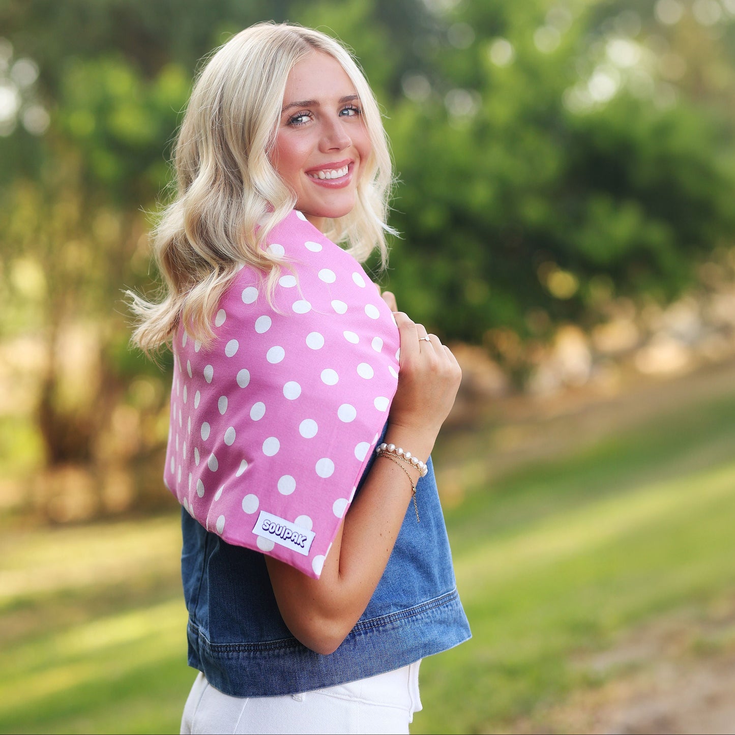 A woman outdoors holding a pink baby carrier with white polka dots. 